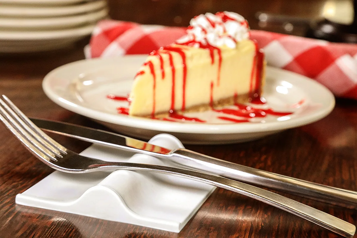 A fork and knife resting on the white LIFSTR utensil rest beside a slice of cheesecake.