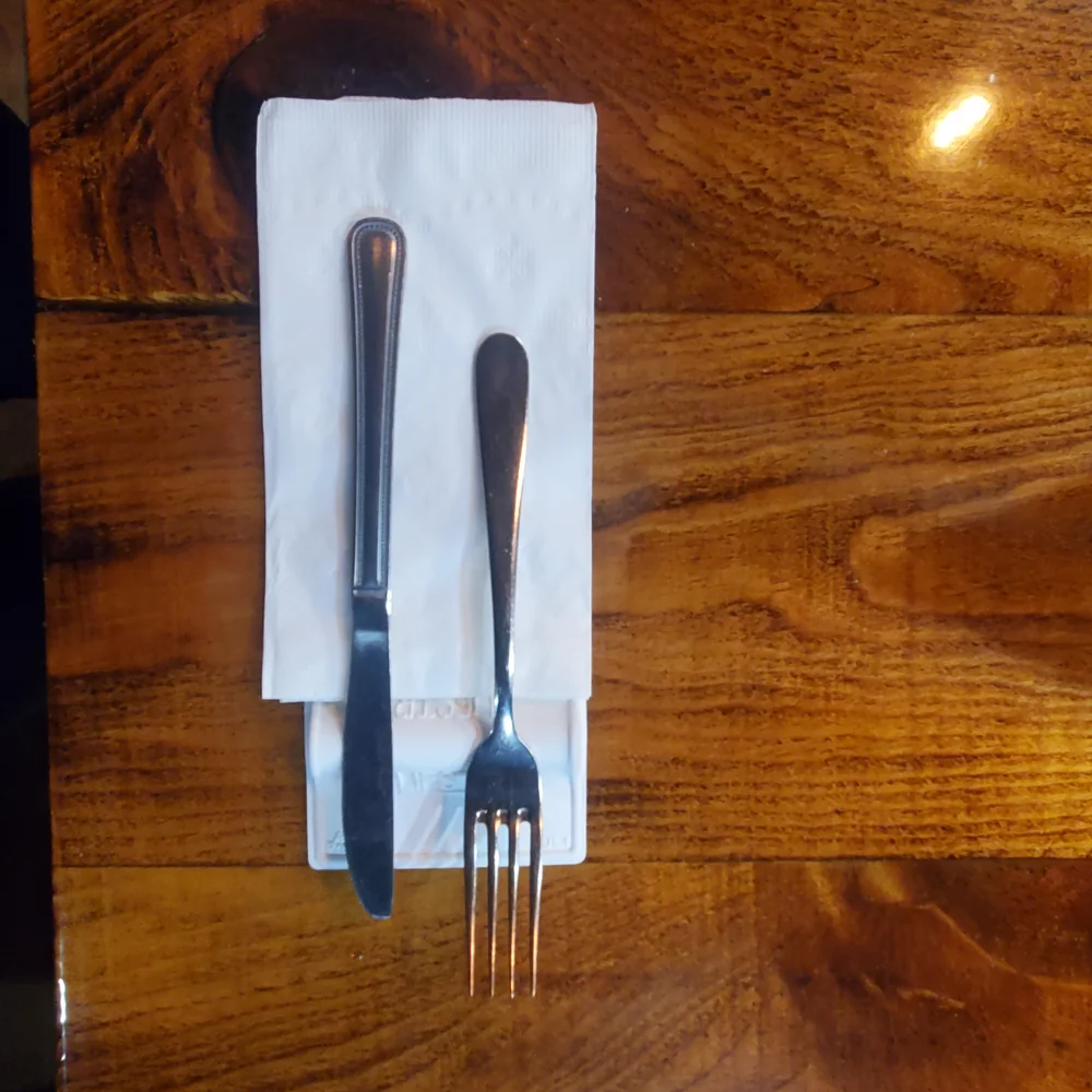 An overhead photo of a white LIFSTR holding a knife and fork beside a folded napkin on a wooden table.