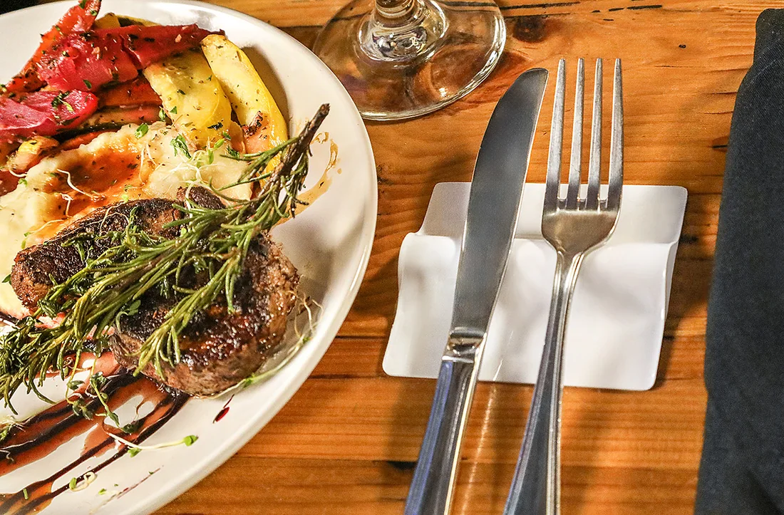 A white LIFSTR holding a knife and fork beside a steak dinner.